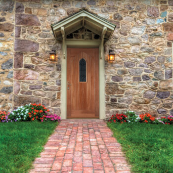Path and door entrance of a stone home with spring flowers and lush lawn.